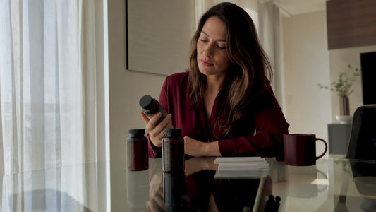 Woman evaluating supplement bottles at kitchen table